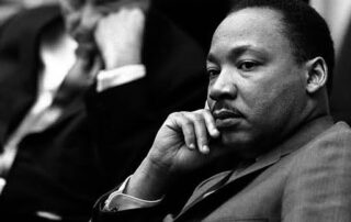 Black and white photograph of Dr. Martin Luther King Jr. in contemplative pose with hand to chin